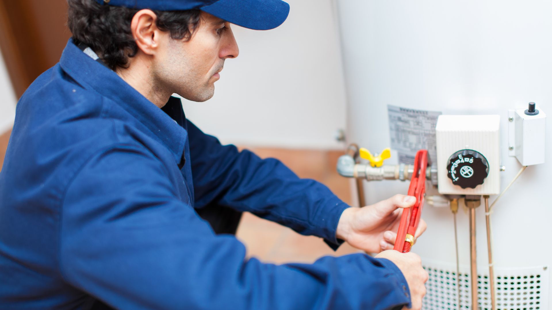 Technician in blue uniform adjusting water heater with red wrench