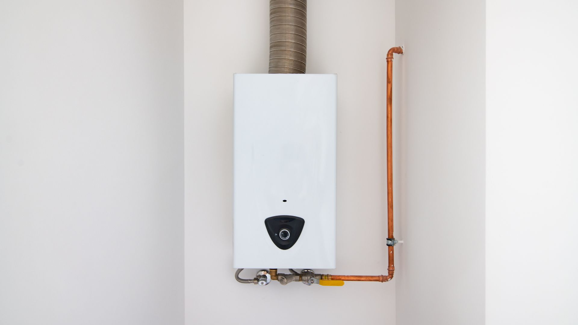 White tankless water heater mounted on wall with copper pipes