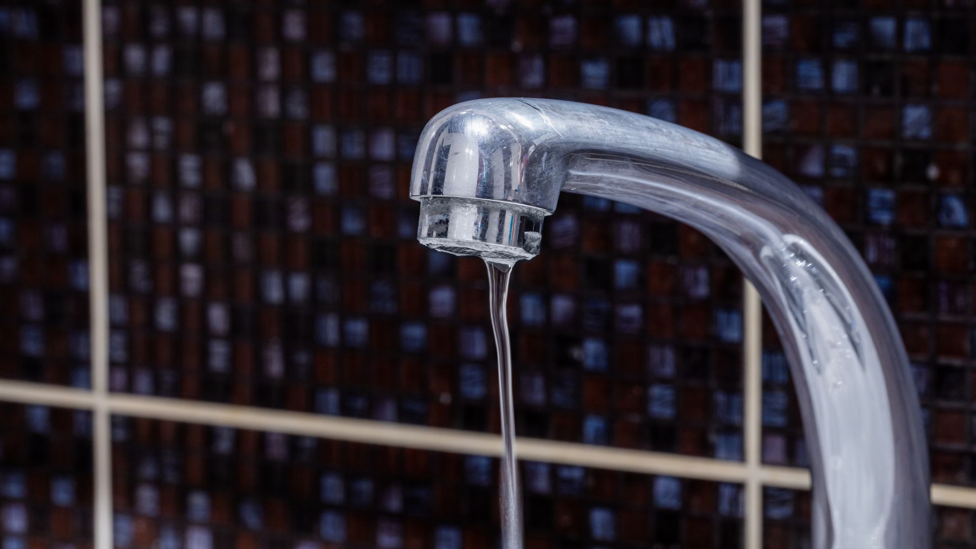 Close-up of running water from a metallic faucet against tiled background