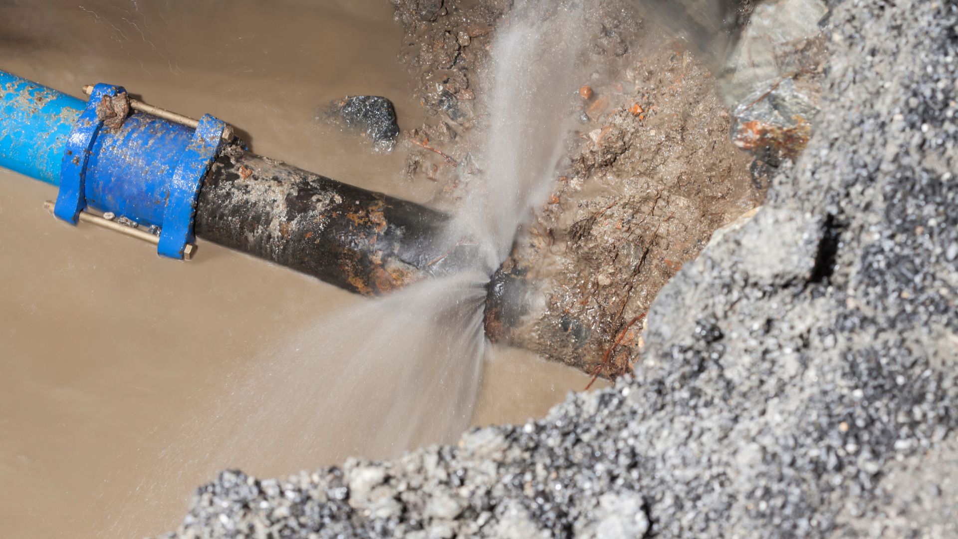 Water bursting from corroded pipe surrounded by gravel and rocks