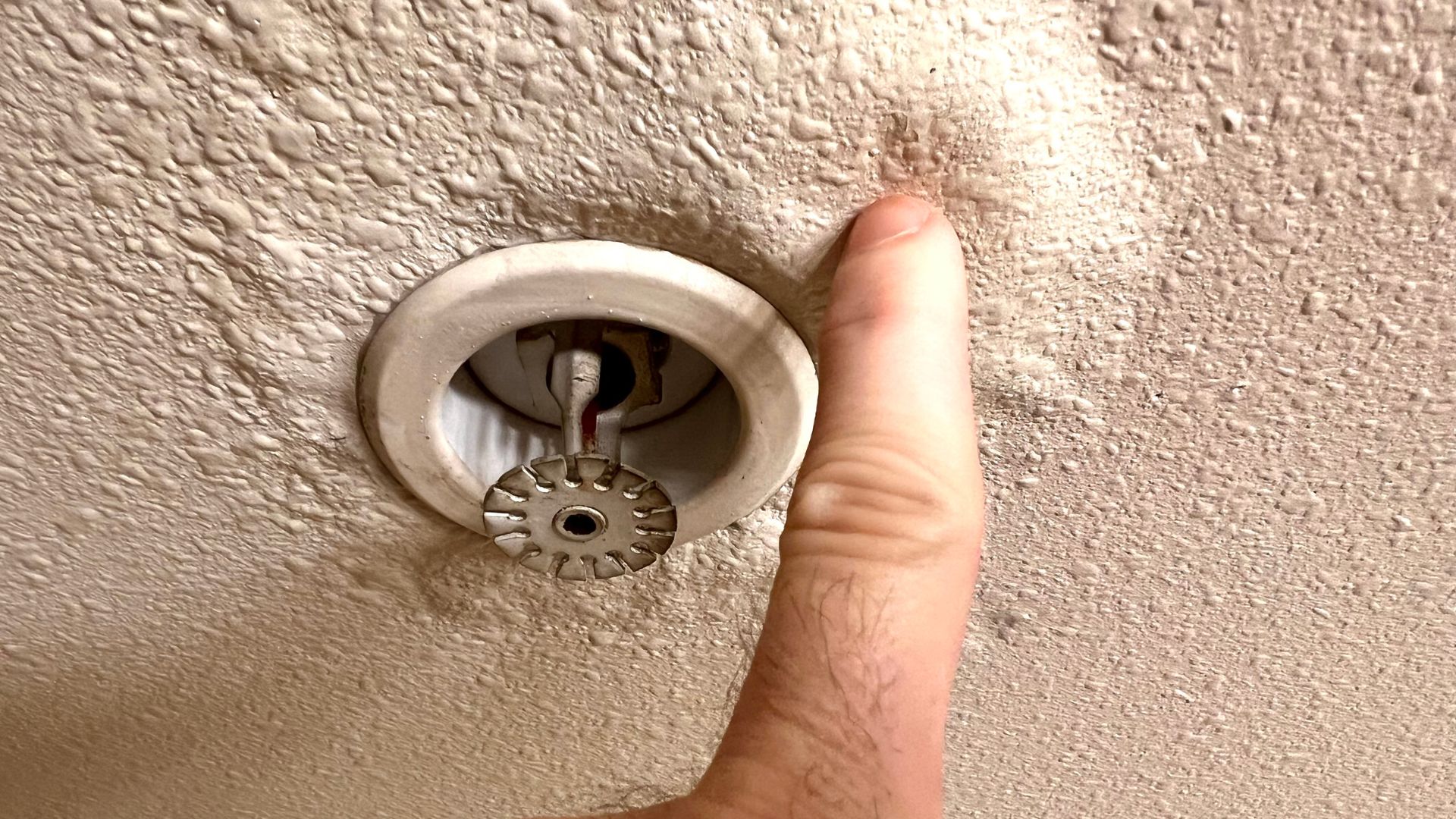 Ceiling fire sprinkler with finger pointing near its metallic head
