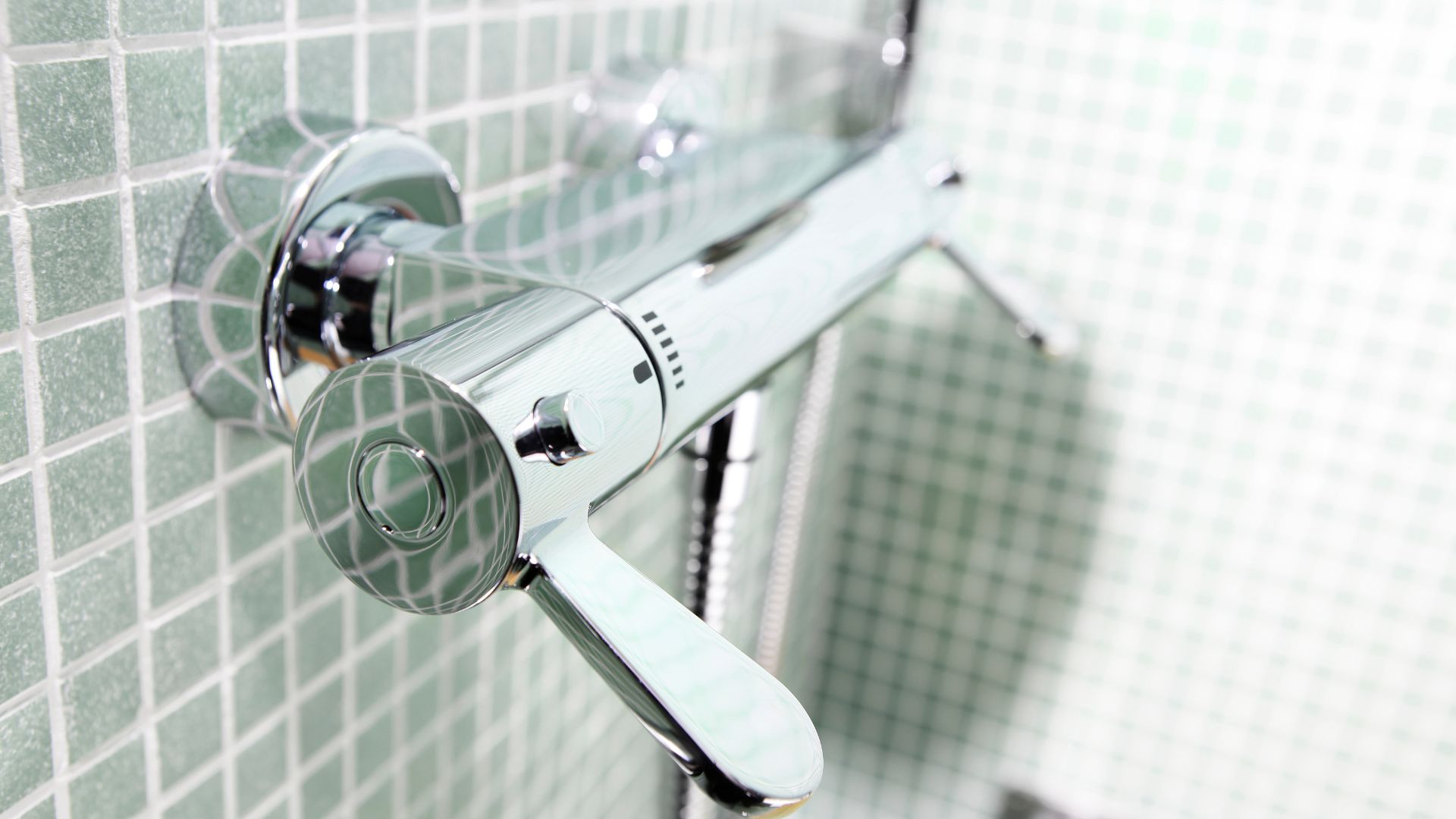 Chrome shower head attached to green tiled bathroom wall