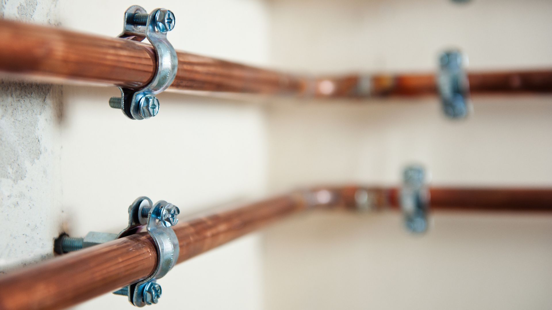 Copper pipes mounted on wall with metal pipe clamps